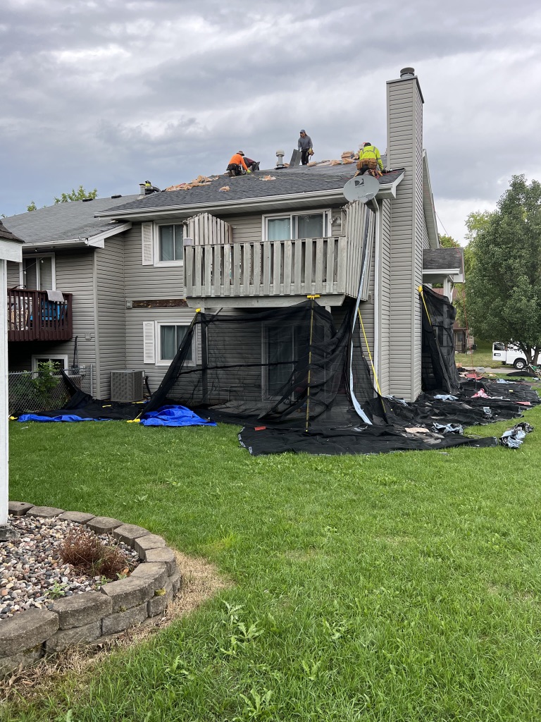 MBE crew tearing off shingles on an Eden Prairie townhome with debris netting protecting the yard