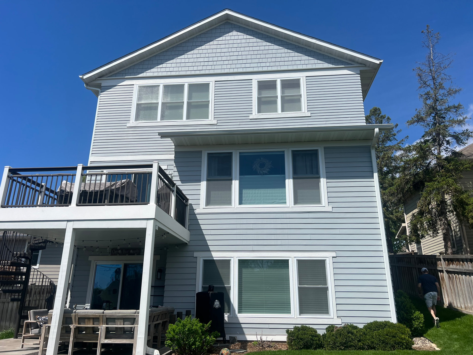 Three-story Edina home with light blue lap siding, shake gable and white trim behind a two-level deck