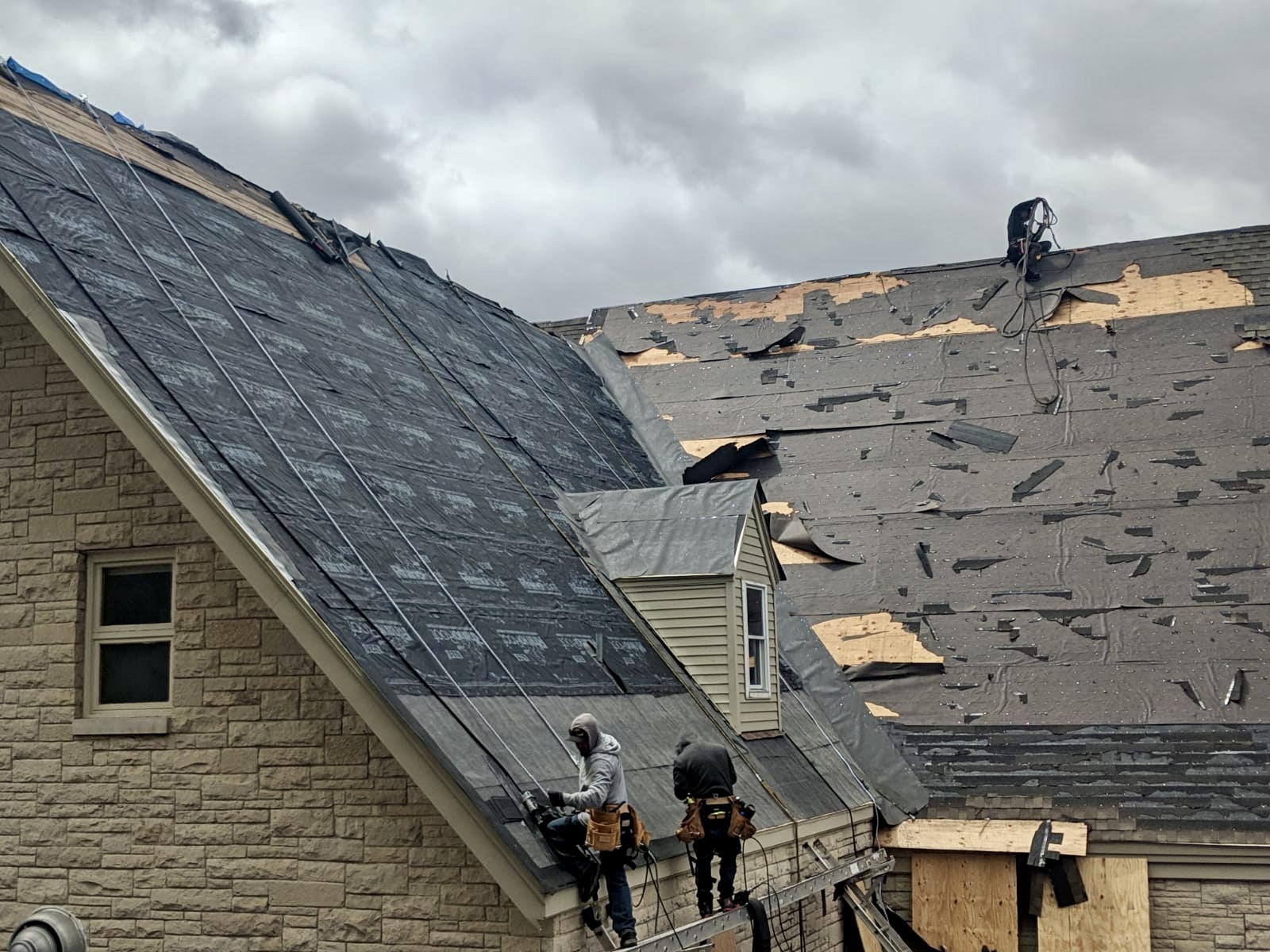 MBE crew tearing off storm-damaged shingles on a steep church roof