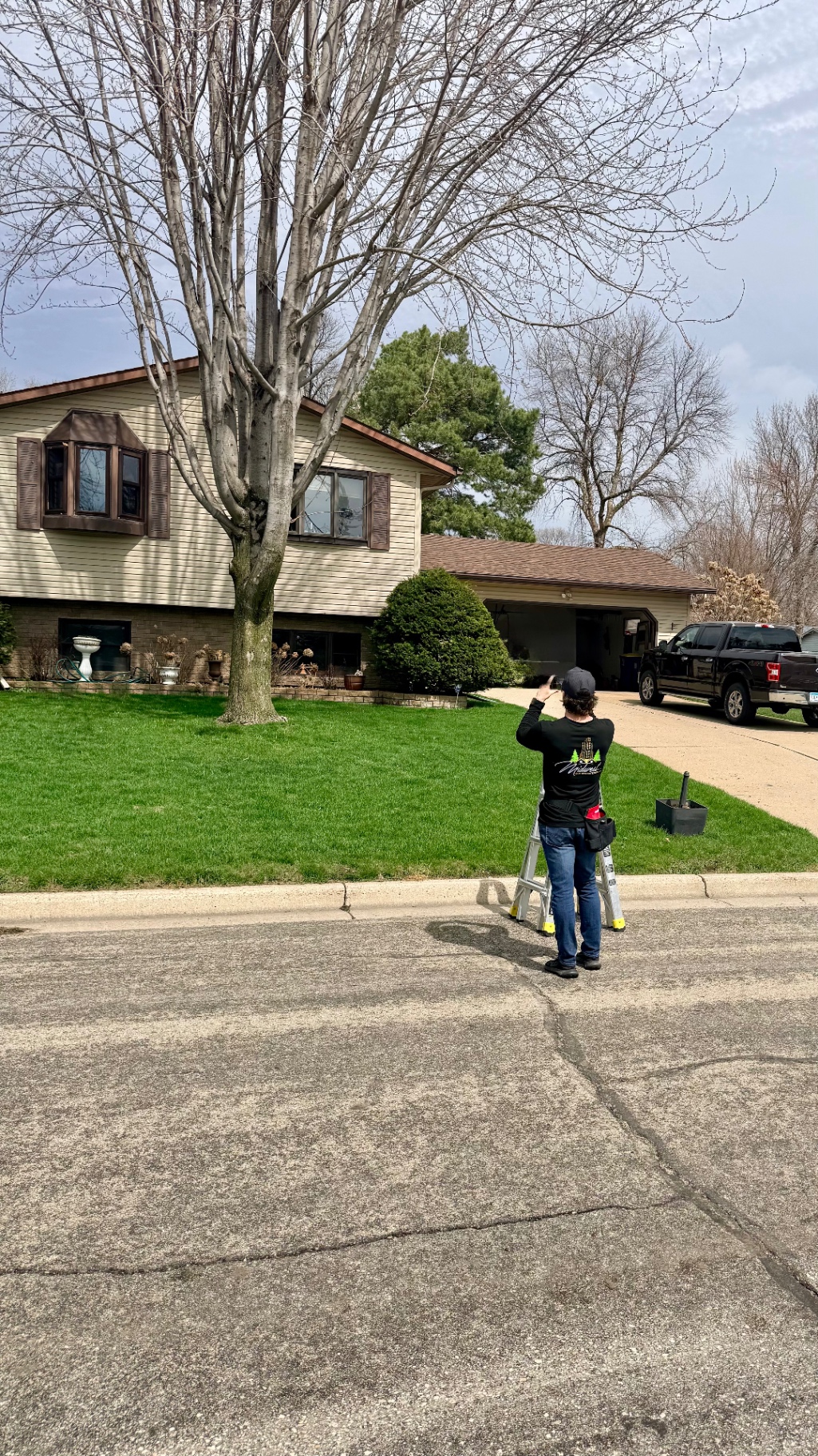Insurance claim site inspection with MBE team member documenting exterior conditions from ladder in front yard — South Metro, MN